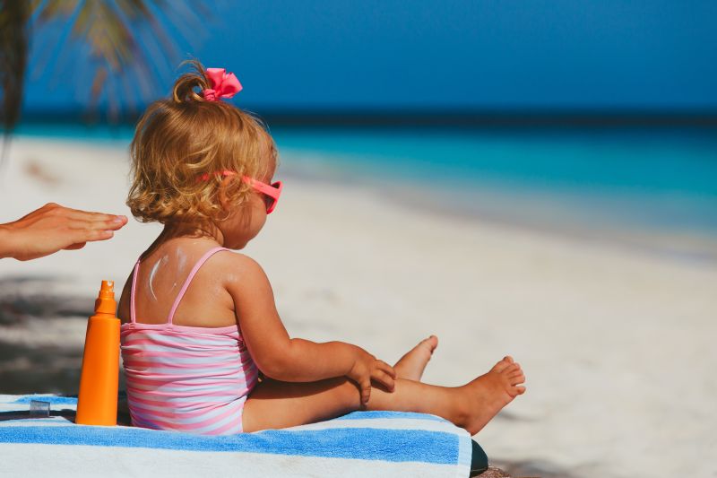 mother applying sunblock cream on daughter shoulder, sun protection